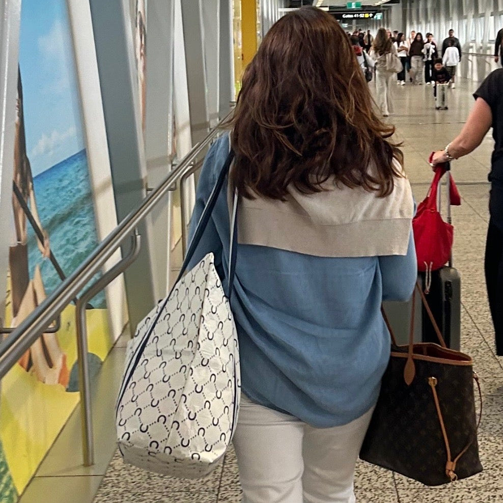 Woman walking through an airport terminal with the Large Zip Tote bag in Navy Horseshoe
- Project Ten