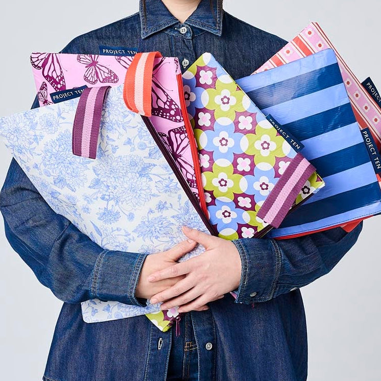 A person holding the Large Zip Pouches. Wallpaper, Butterfly, Toile, Mosaic and Blue Stripe.
- Project Ten