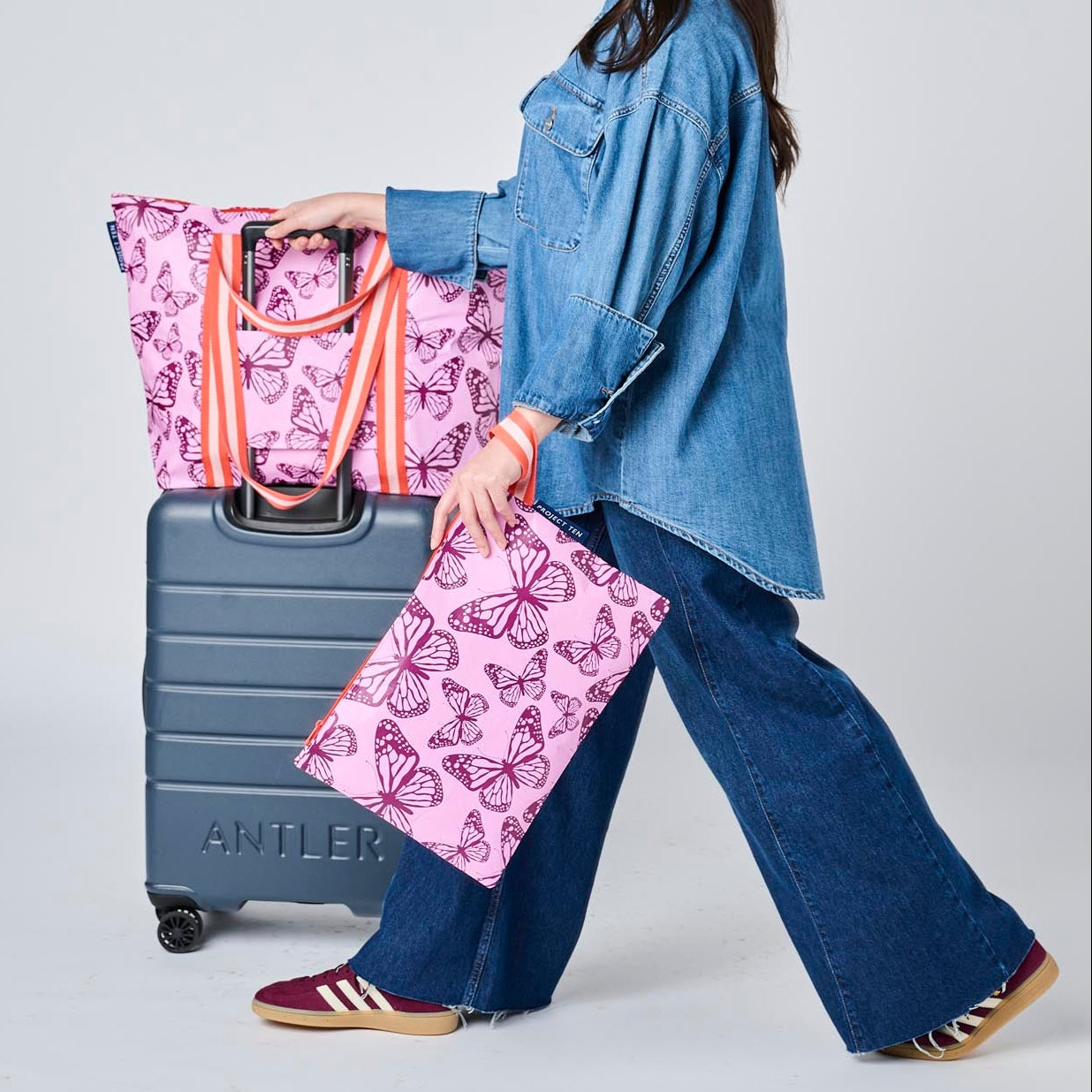 Someone walking with a suitcase and the Zip Medium Tote using the luggage band. They are also holding the Large Zip Pouch in their hand,
- Project Ten