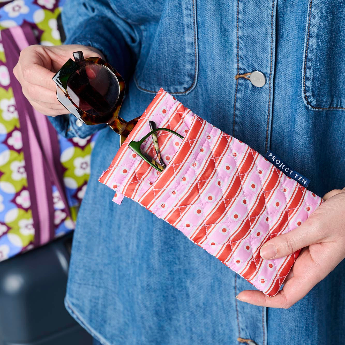 Someone placing sunglasses in the top pocket of the glasses case. Reading glasses are in the front pocket.
- Project Ten