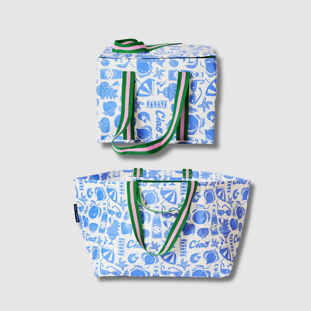 Our Feast Beach Large Shopping Bundle, a zip-top Large Insulated Tote and Oversized Tote in an ecru base with a blue seaside print of shells, lemons, sunglasses, beach umbrellas and "Ciao" lettering, each with green and pink striped carry handles.