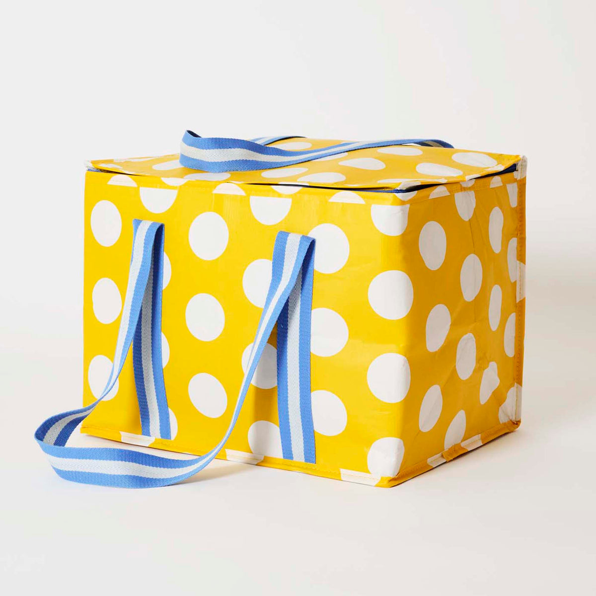 Our Yellow Polka Dot Large Insulated Tote, a large boxy cooler bag in bright yellow with ecru polka dots, with a fold-over zip lid, long blue and ecru striped shoulder straps and a short blue and ecru striped top handle.