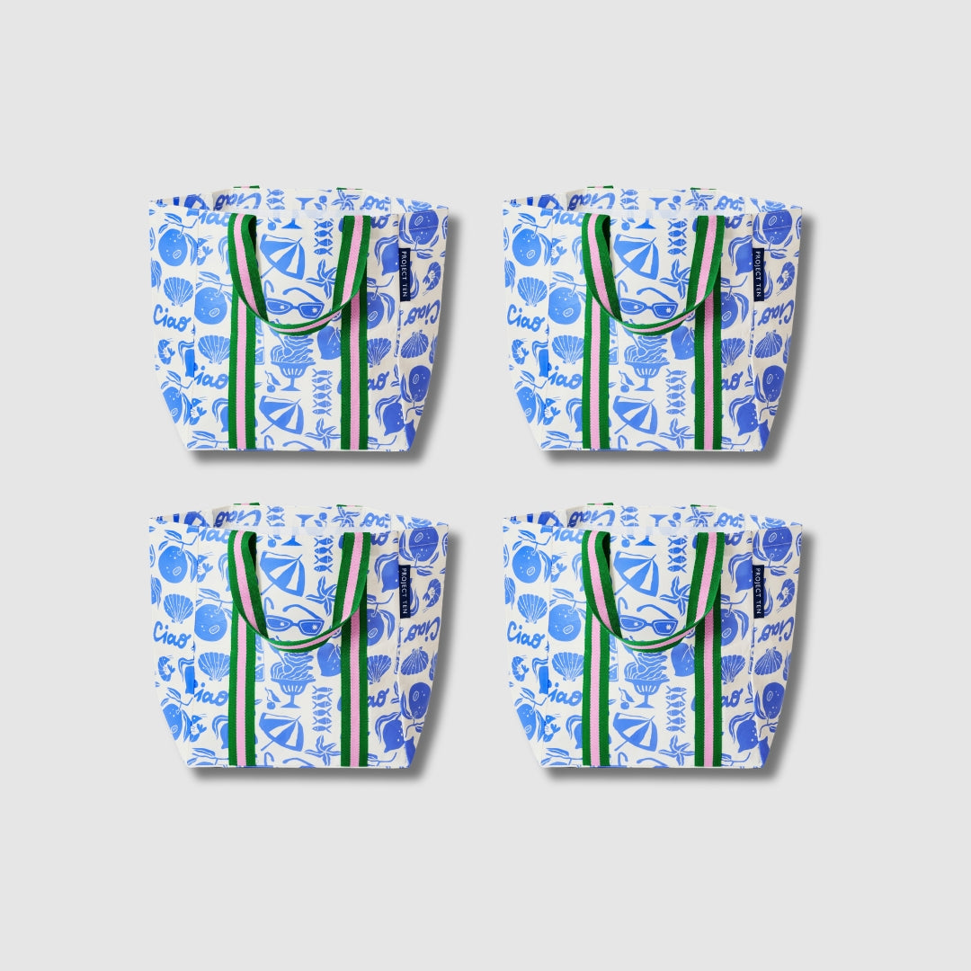 Our Feast Shopper Tote Bundle, a set of four Shopper Totes in an ecru base with a blue seaside print of shells, oranges, sunglasses, beach umbrellas and "Ciao" lettering, each with green and pink striped carry handles.