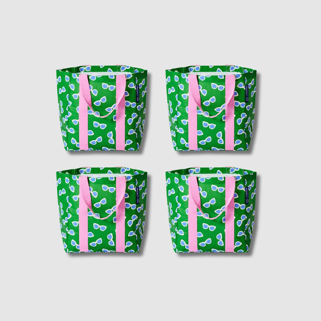 Our Sunglasses Shopper Tote Bundle, a set of four Shopper Totes in green with a scattered print of blue-lensed, white-framed sunglasses, each with pink carry handles.