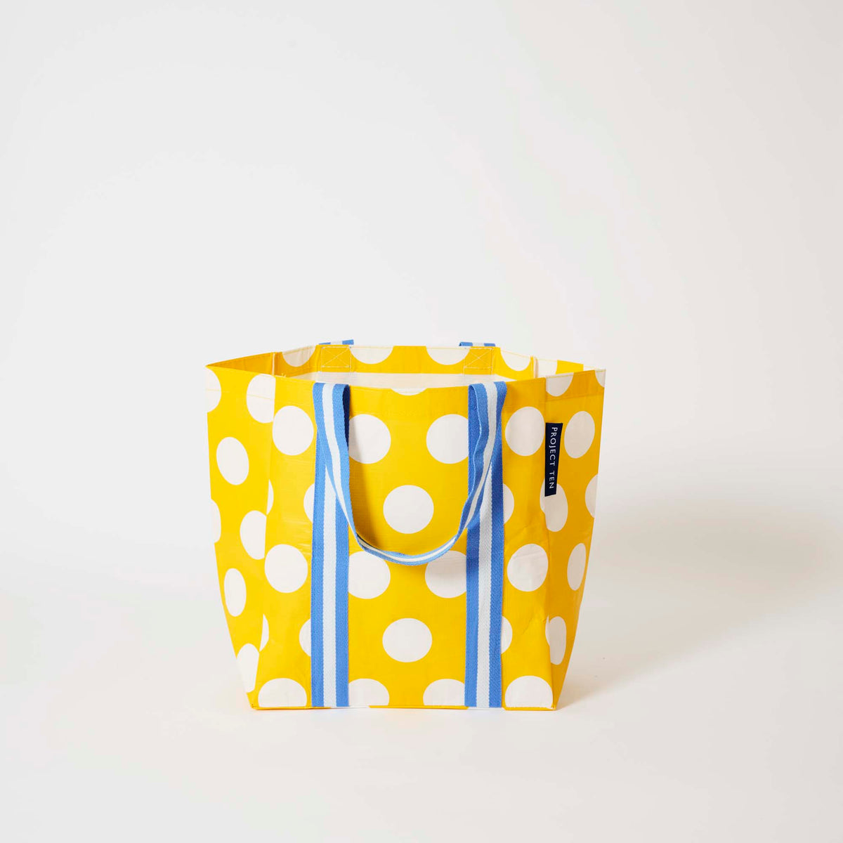 Our Yellow Polka Dot Shopper Tote in bright yellow with ecru polka dots and blue and ecru striped straps that run down the front and back, shown open against a plain background.
