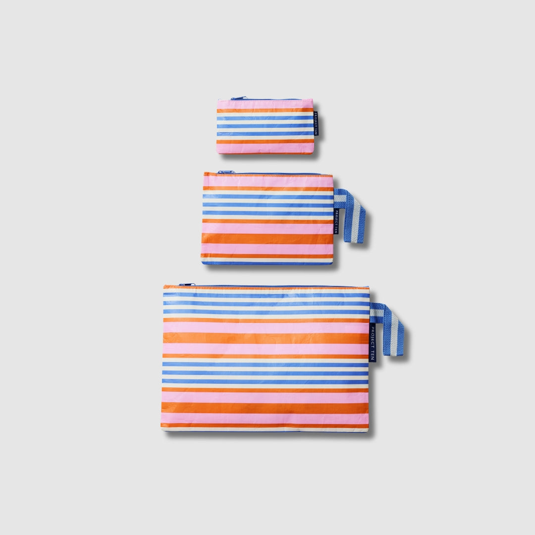 Our Capri Stripe Zip Pouch Bundle, a set of three Zip Pouches in small, medium and large in pink, orange, blue and ecru stripes, with blue and ecru striped loop tabs on the medium and large pouches.