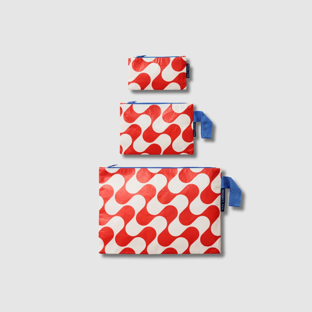 Our Red Ripple Zip Pouch Bundle, a set of three Zip Pouches in small, medium and large in a bold geometric wave print of red and ecru, with blue loop tabs on the medium and large pouches.