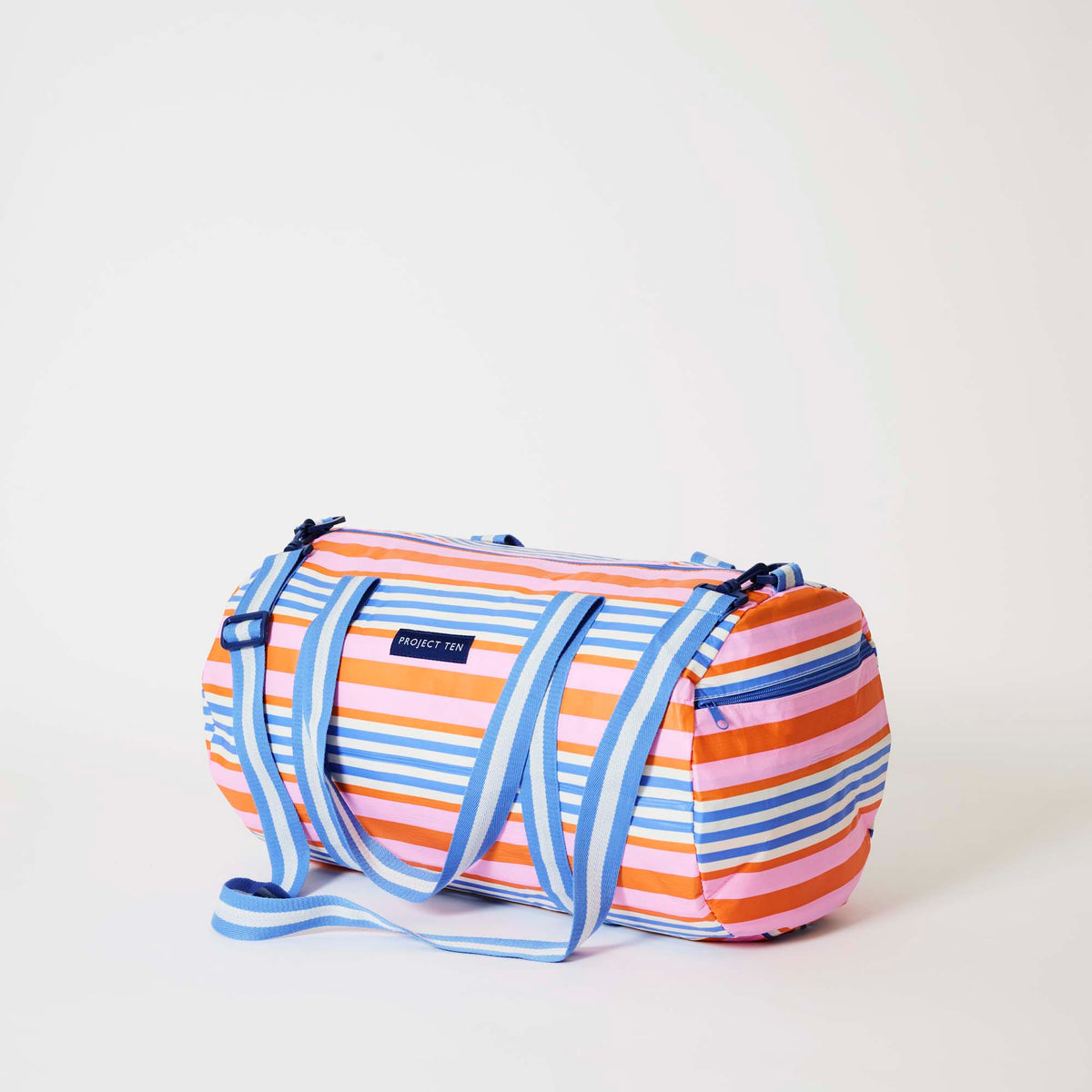 Our Capri Stripe Barrel Bag, a cylindrical duffle-style bag in pink, orange, blue and ecru horizontal stripes, with two blue and ecru striped carry handles, a detachable matching shoulder strap and a blue zip.