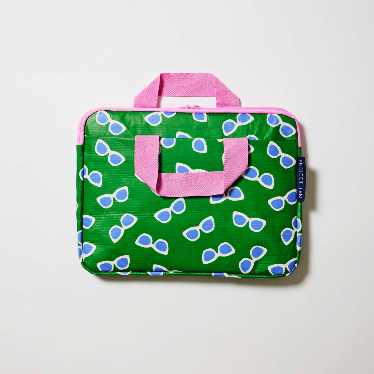 Our Sunglasses Laptop Case, a slim zip-up laptop case in green with a scattered print of blue-lensed, white-framed sunglasses, two pink carry handles and a pink zip.