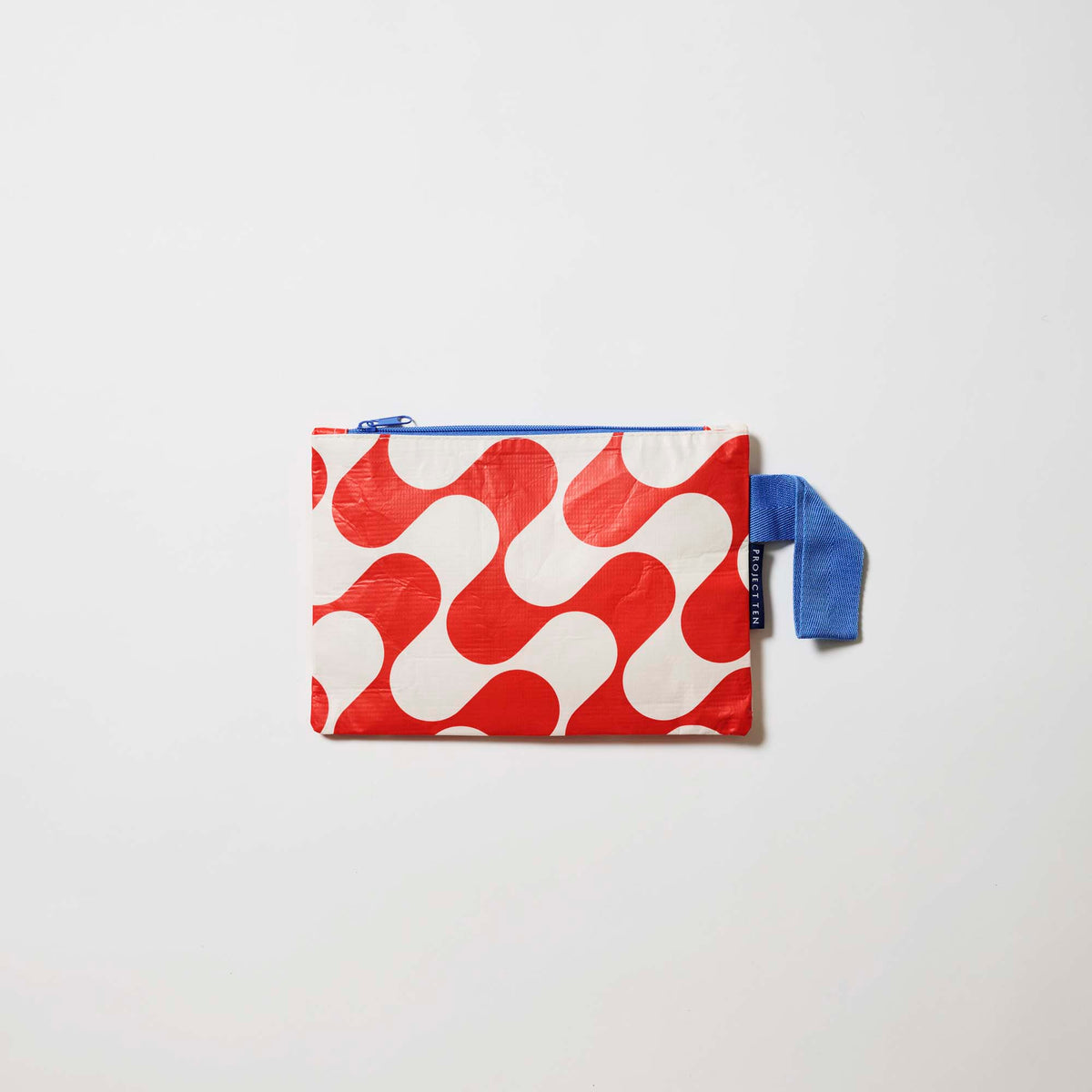 Red Ripple Mini Zip Pouch
Our Red Ripple Mini Zip Pouch, a small rectangular pouch in a red and ecru wave print with a blue zip and blue handle.