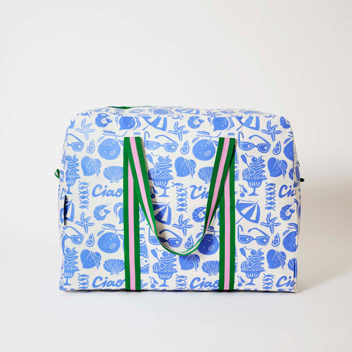 Our Feast Overnight Bag, a roomy duffle-style bag in an ecru base with a blue seaside print of sunglasses, ice cream sundaes, oranges, shells, sardines and "Ciao" lettering, with two green and pink striped carry handles and a green zip.