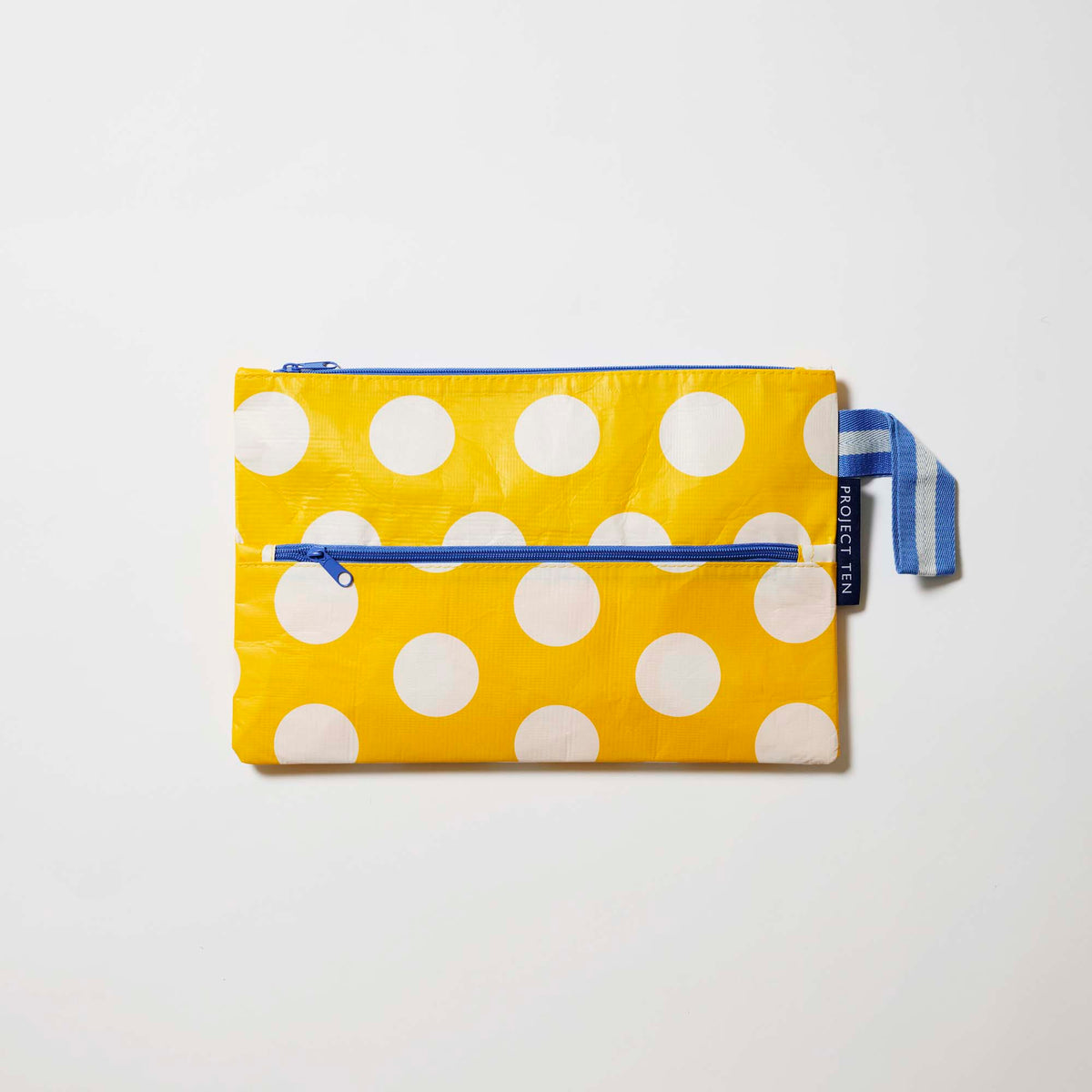 Our Yellow Polka Dot Pencil Case, a flat rectangular case in bright yellow with ecru polka dots, two blue zip compartments and a blue and ecru striped handle.