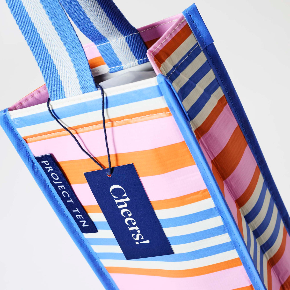 Our Capri Stripe Wine Bag, a tall narrow bottle bag in pink, orange, blue and ecru horizontal stripes with a blue trim and a single blue and ecru striped carry handle.