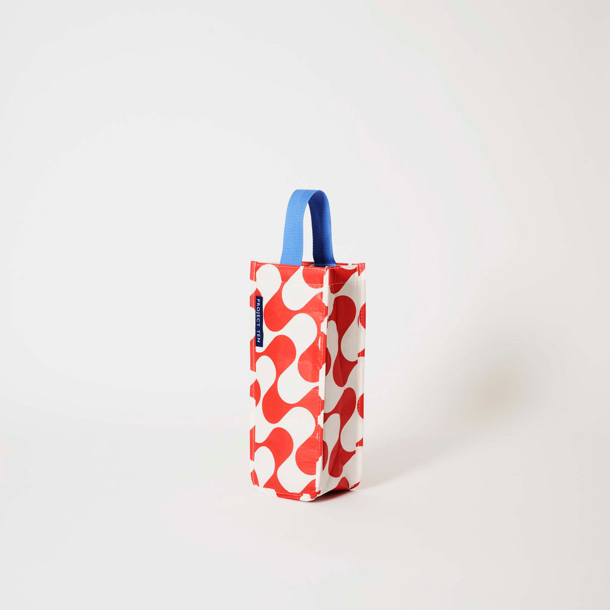 Our Red Ripple Wine Bag, a tall narrow bottle bag in a red and ecru wave print with a single blue carry handle.