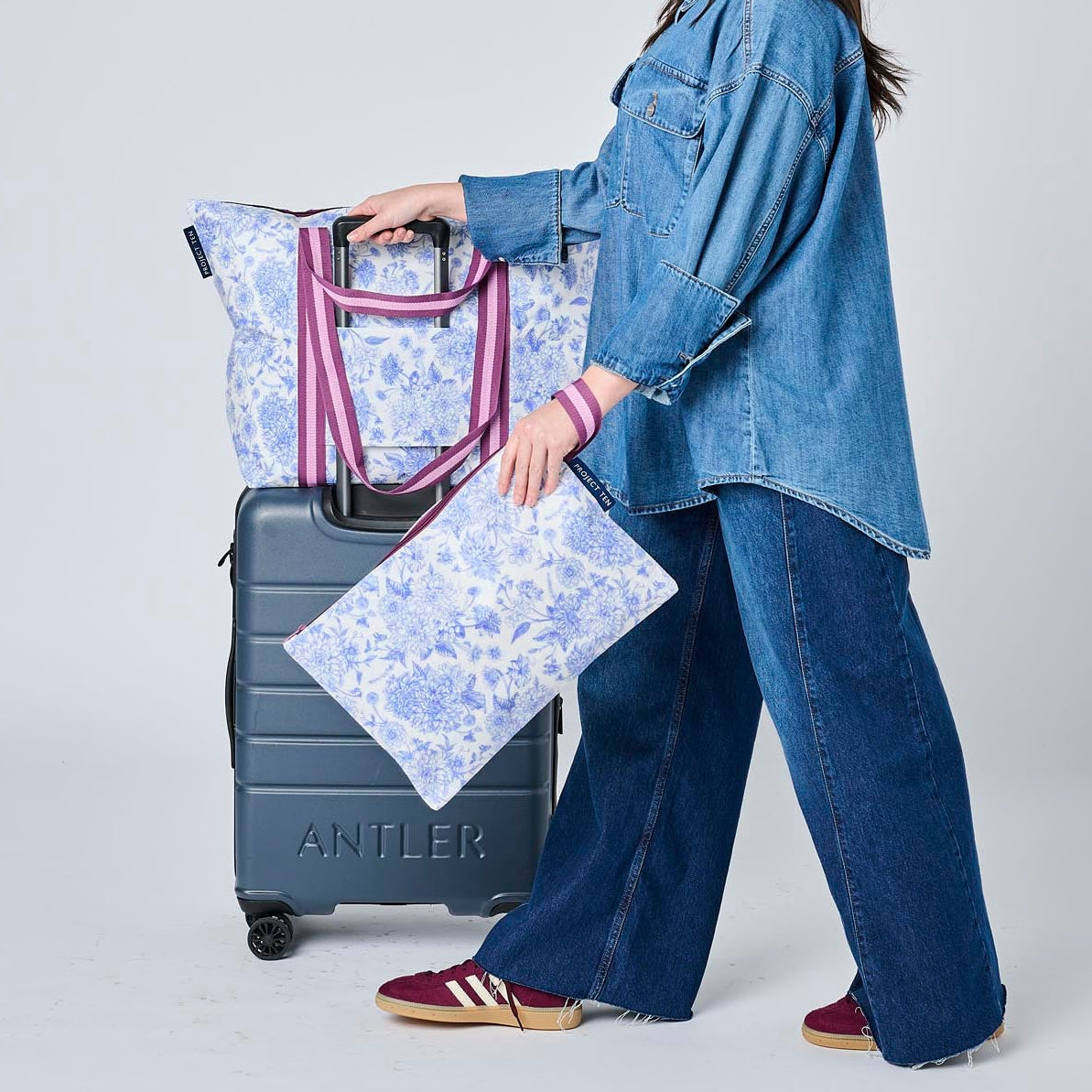 Someone pushing a suitcase with the Zip Medium Tote on top using the luggage band. 
They are holding a Large Zip Pouch in their hand. 
- Project Ten