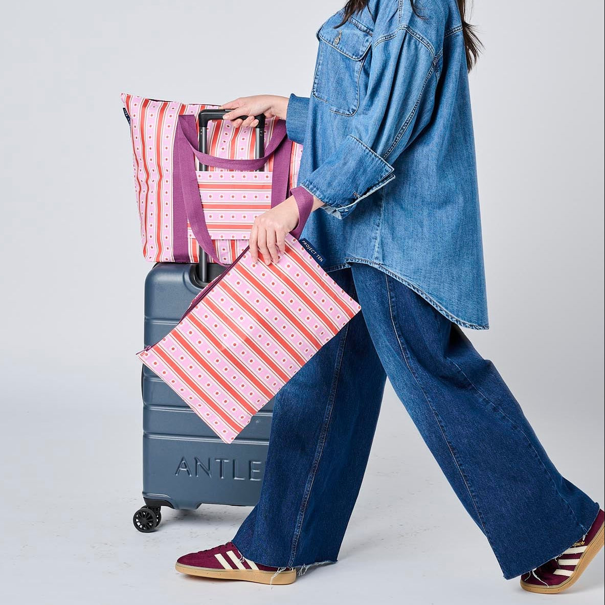 Our Zip Medium Tote on top of the suitcase using the luggage band. 
She is holding our Large Zip Pouch in her hand, all in Wallpaper
- Project Ten