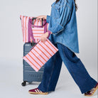Our Zip Medium Tote on top of the suitcase using the luggage band. 
She is holding our Large Zip Pouch in her hand, all in Wallpaper
- Project Ten