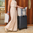 Someone pushing a suitcase with a Medium Zip Tote using the luggage band. 
In the other hand they are holding a Large Zip Pouch. Both are in Navy Horseshoe pattern. 