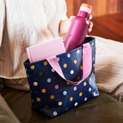 Person holding a pink drink bottle in a Mini Tote – Confetti 
Polka dots on navy background- Project Ten