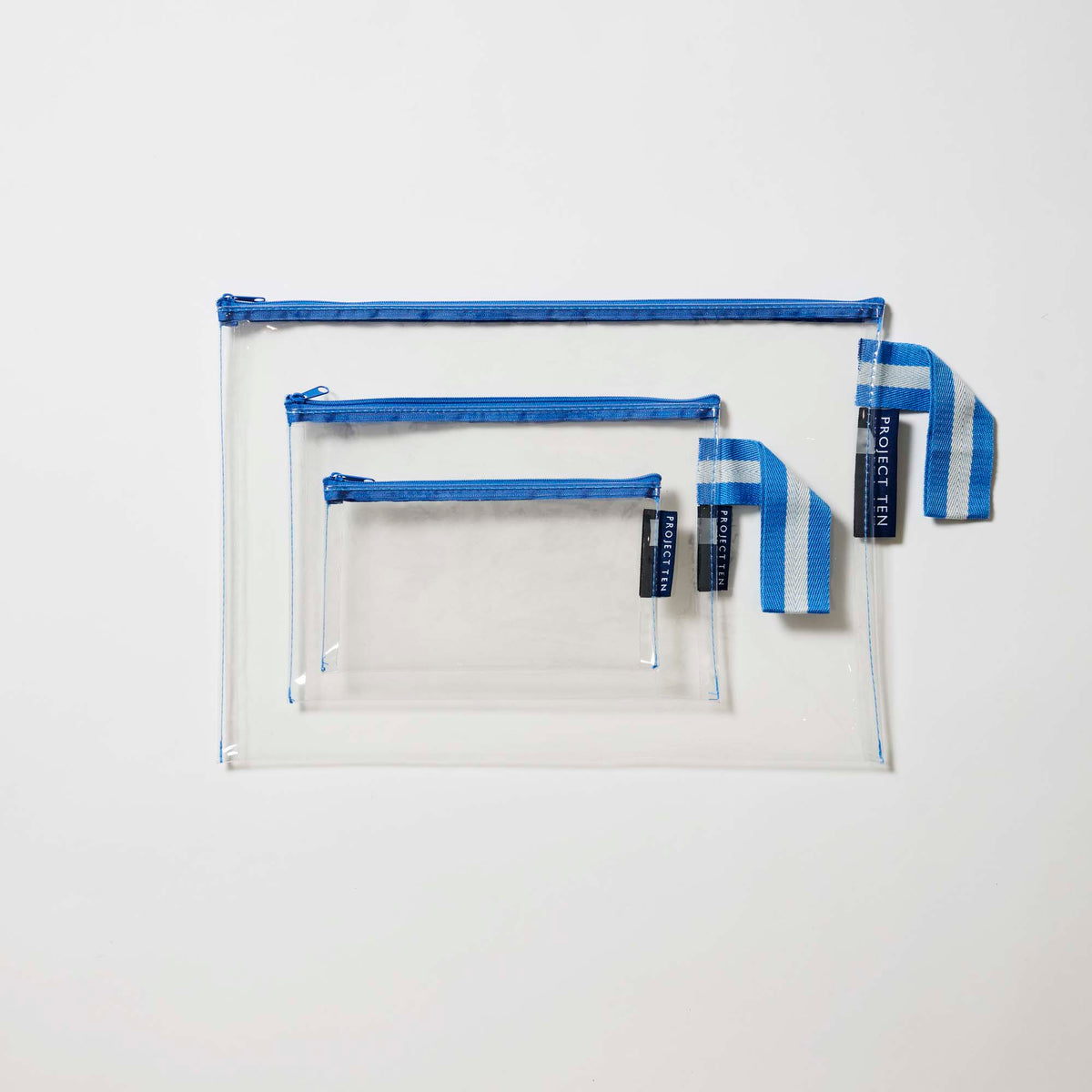 Our Blue Clear Zip Pouch Bundle, a set of three clear zip pouches in small, medium and large, with blue zips and blue and ecru striped loop tabs.