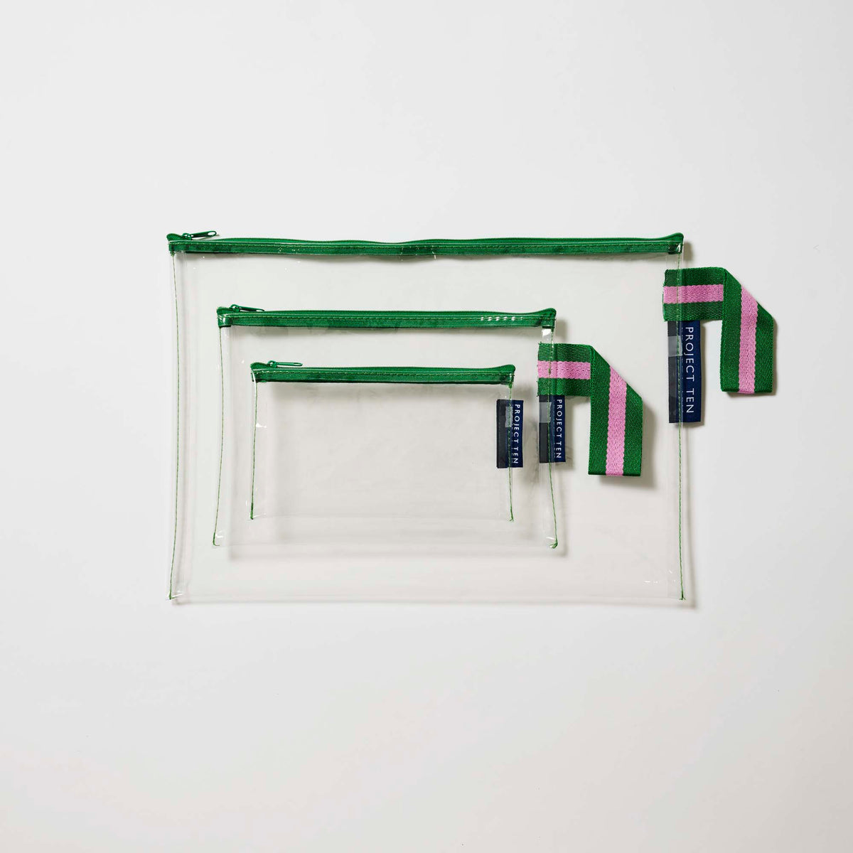Our Green Clear Zip Pouch Bundle, a set of three clear zip pouches in small, medium and large, with green zips and green and pink striped loop tabs.
