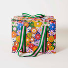 Our Coastal Floral Large Insulated Tote, a large boxy cooler bag covered in bright retro daisies in orange, pink, yellow and blue on a navy background, with a fold-over zip lid, long green and pink striped shoulder straps and a short green and pink striped top handle.
