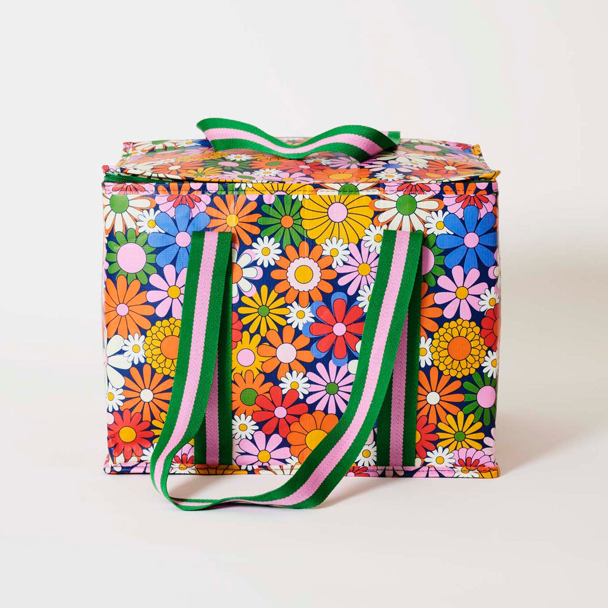 Our Coastal Floral Large Insulated Tote, a large boxy cooler bag covered in bright retro daisies in orange, pink, yellow and blue on a navy background, with a fold-over zip lid, long green and pink striped shoulder straps and a short green and pink striped top handle.