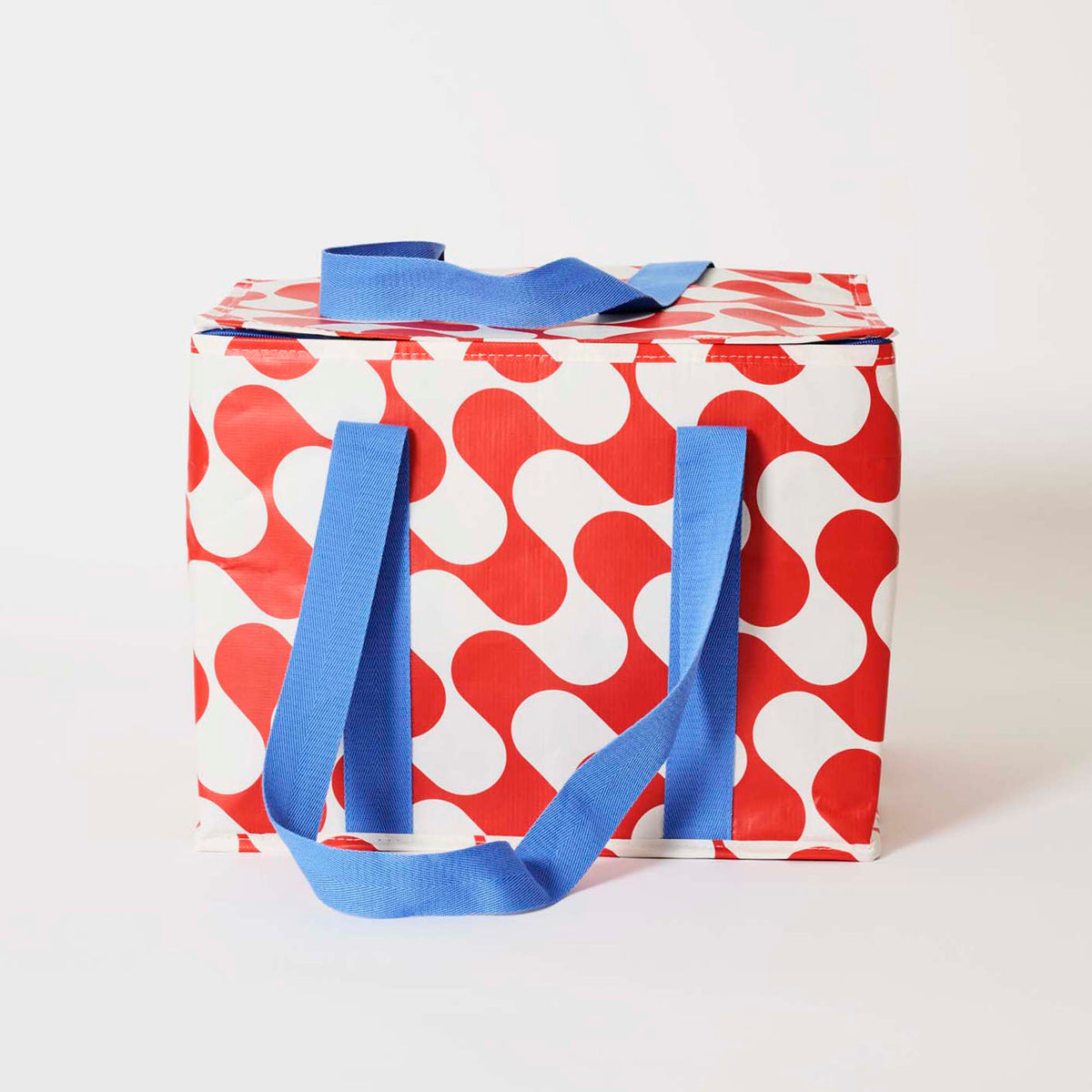 Our Red Ripple Large Insulated Tote, a large boxy cooler bag in a red and ecru wave print with a fold-over zip lid, long blue shoulder straps and a short blue top handle.