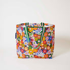 Our Coastal Floral Medium Tote covered in bright retro daisies in orange, pink, yellow and blue on a navy background, with green and pink striped straps, shown open against a plain background.