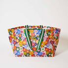 Our Coastal Floral Oversized Tote covered in bright retro daisies in orange, pink, yellow and blue on a navy background, with green and pink striped straps, shown open against a plain background.