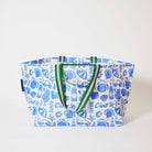 Our Feast Oversized Tote in a blue and ecru print of lemons, seafood, gelato, soda bottles, sunglasses, beach umbrellas and the word "Ciao", with green and pink striped straps, shown open against a plain background.
