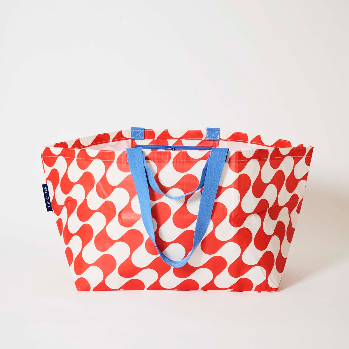 Our Red Ripple Oversized Tote in a red and cream wave print with blue straps, shown open against a plain background.