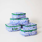 Our Feast Packing Cubes, a set of five zip-up packing cubes in different sizes, in an ecru base with a blue seaside print of shells, oranges, soda bottles, sunglasses and "Ciao" lettering, with green zips and green and pink striped carry handles.