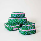 Our Sunglasses Packing Cubes, a set of five zip-up packing cubes in different sizes, in green with a scattered print of blue-lensed, white-framed sunglasses, with pink zips and pink carry handles.