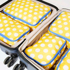 Our Yellow Polka Dot Packing Cubes, a set of five zip-up packing cubes in different sizes, in bright yellow with large ecru polka dots, with blue zips and blue and ecru striped carry handles.