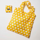 Our Yellow Polka Dot Pocket Shopper, a lightweight foldable tote in bright yellow with ecru polka dots, shown open and laid flat next to its matching pouch that it folds into with a snap closure.
