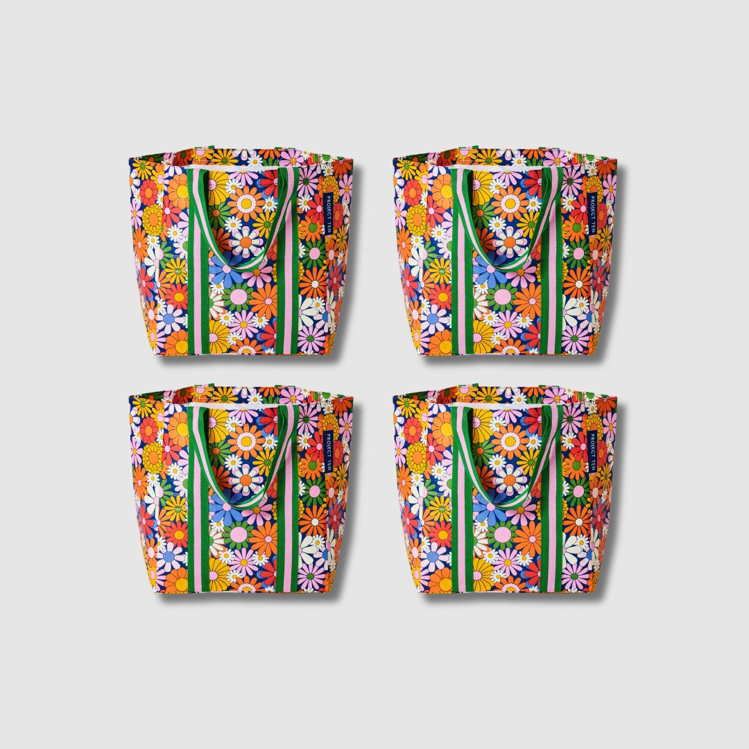Our Coastal Floral Shopper Tote Bundle, a set of four Shopper Totes in a retro daisy print of orange, red, pink, yellow, blue and white flowers on a navy background, each with green and pink striped carry handles.