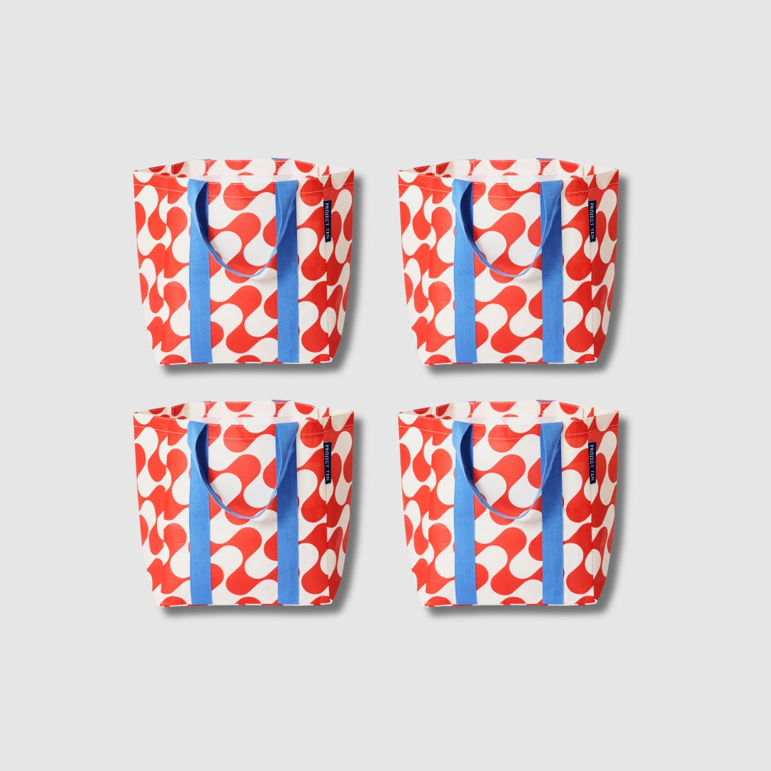 Our Red Ripple Shopper Tote Bundle, a set of four Shopper Totes in a bold geometric wave print of red and ecru, each with blue carry handles.