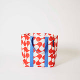 Our Red Ripple Shopper Tote in a red and ecru wave print with blue straps that run down the front and back, shown open against a plain background.