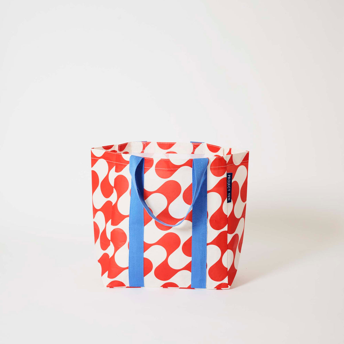 Our Red Ripple Shopper Tote in a red and ecru wave print with blue straps that run down the front and back, shown open against a plain background.