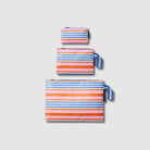 Our Capri Stripe Zip Pouch Bundle, a set of three Zip Pouches in small, medium and large in pink, orange, blue and ecru stripes, with blue and ecru striped loop tabs on the medium and large pouches.
