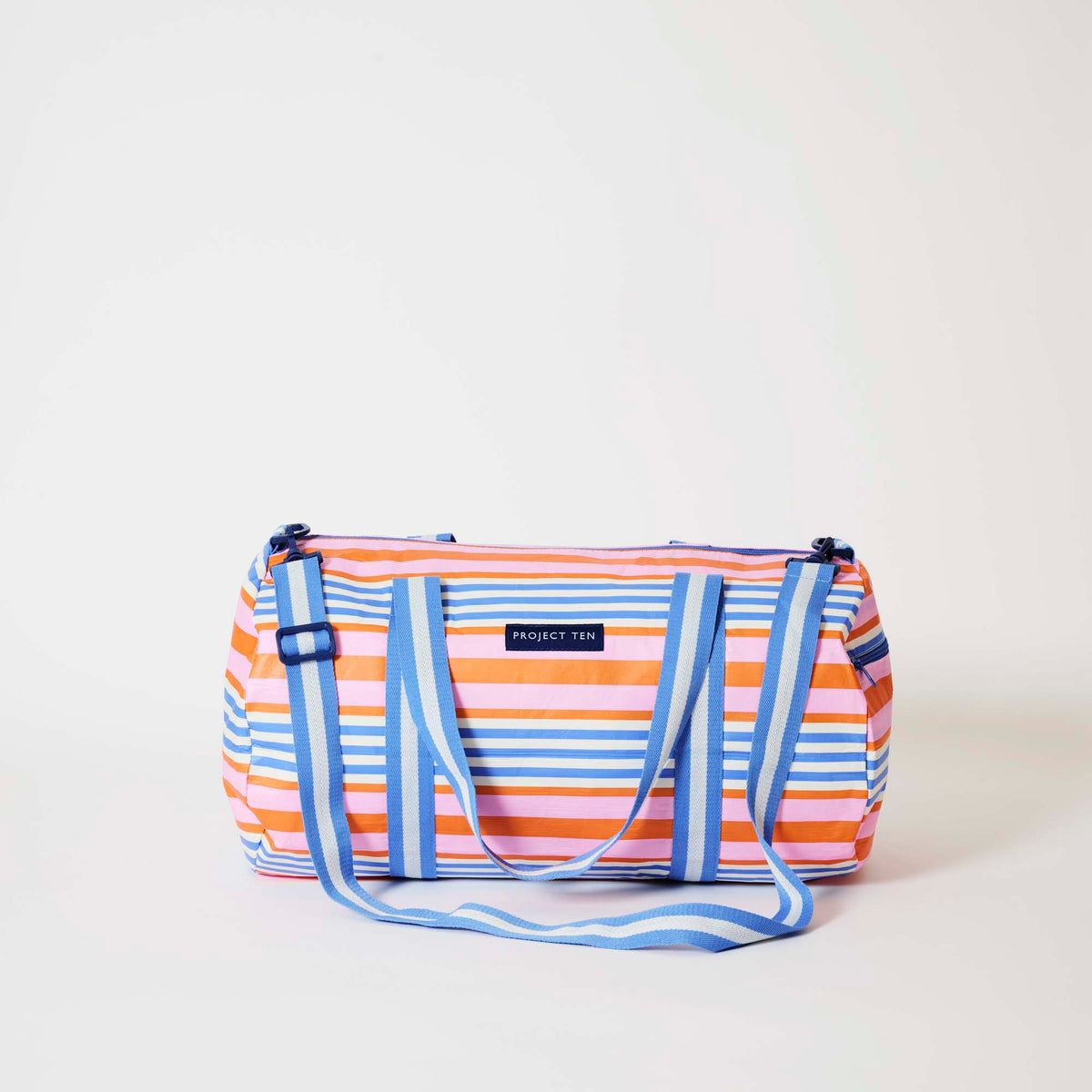 Our Capri Stripe Barrel Bag, a cylindrical duffle-style bag in pink, orange, blue and ecru horizontal stripes, with two blue and ecru striped carry handles, a detachable matching shoulder strap and a blue zip.