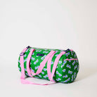 Our Sunglasses Barrel Bag, a cylindrical duffle-style bag in green with a scattered print of blue-lensed, white-framed sunglasses, two pink carry handles, a detachable pink shoulder strap and a pink zip.