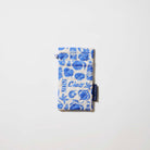 Our Feast Double Glasses Case, a soft quilted glasses case in an ecru base with a blue seaside print of shells, sardines, oranges, soda bottles and "Ciao" lettering, with a squeeze-top opening and a small loop tab.