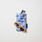 Our Feast Double Glasses Case, a soft quilted glasses case in an ecru base with a blue seaside print of shells, sardines, oranges, soda bottles and "Ciao" lettering, with a squeeze-top opening and a small loop tab.