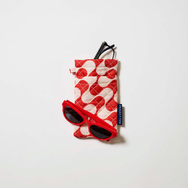 Our Red Ripple Double Glasses Case, a soft quilted glasses case in a bold geometric wave print of red and ecru, with a squeeze-top opening and a small loop tab.