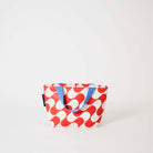 Our Red Ripple Mini Tote, a compact tote bag in a bold geometric wave print of red and ecru, with two blue carry handles.