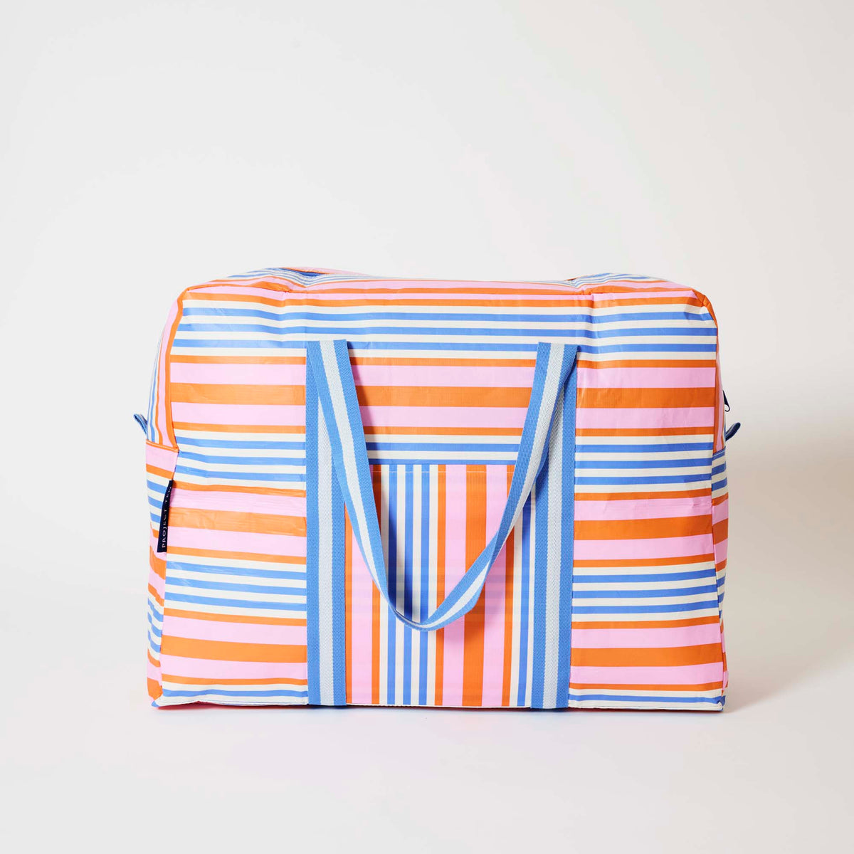 Our Capri Stripe Overnight Bag, a roomy duffle-style bag in pink, orange, blue and ecru stripes, with a vertical striped front pocket, two blue and ecru striped carry handles and a blue zip.
