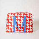Our Red Ripple Overnight Bag, a roomy duffle-style bag in a bold geometric wave print of red and ecru, with two blue carry handles and a blue zip.