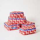 Our Red Ripple Packing Cubes, a set of five zip-up packing cubes in different sizes, in a bold geometric wave print of red and ecru, with blue zips and blue carry handles.